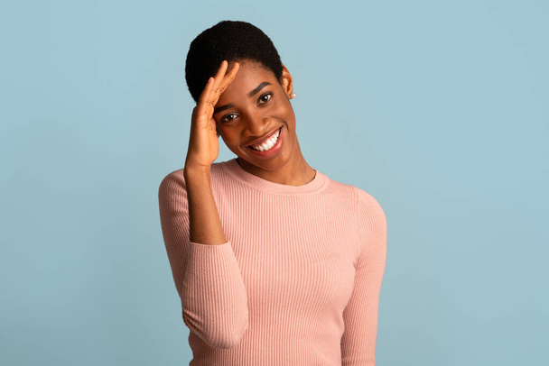 Porträt einer schüchternen Afroamerikanerin, die in peinlicher Weise lächelt und den Kopf berührt - Foto, Bild