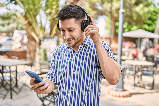 Junger schöner Mann trägt Kopfhörer mit Smartphone im Park - Foto, Bild