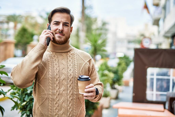 Mladý kavkazský muž mluví na smartphone pití kávy ve městě. - Fotografie, Obrázek
