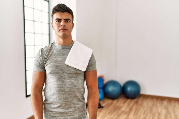 Young hispanic man wearing sportswear and towel at the gym relaxed with serious expression on face. simple and natural looking at the camera.  - Foto, imagen