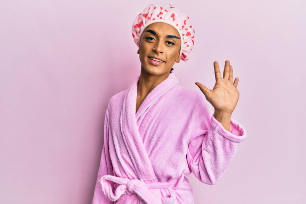 Hispanische Mann mit Make-up trägt Duschtuchmütze und Bademantel zeigt und zeigt mit den Fingern Nummer fünf und lächelt zuversichtlich und glücklich.  - Foto, Bild