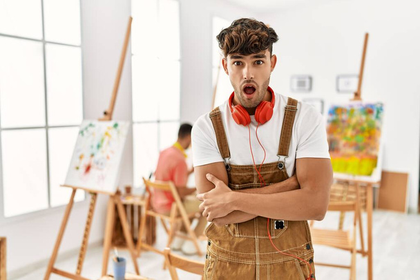 Joven hombre hispano en estudio de arte asustado y sorprendido con la expresión sorpresa, el miedo y la cara emocionada.  - Foto, imagen