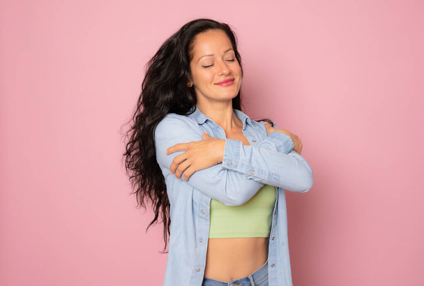 Lifestyle, beauty and women concept. Portrait of carefree, romantic young woman smiling while daydreaming, close eyes and remember moment, hugging herself, standing over pink background - Φωτογραφία, εικόνα