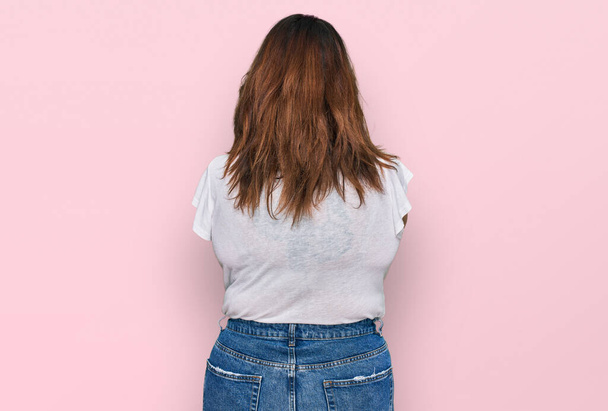 Jovem plus size mulher vestindo casual t-shirt branca de pé para trás olhando para longe com os braços cruzados  - Foto, Imagem