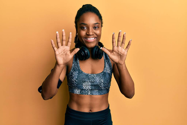 Африканська американка з плетеним волоссям в спортивному плащі і смузі руки показує і вказує вгору з пальцями номер десять, посміхаючись впевнено і щасливо.  - Фото, зображення