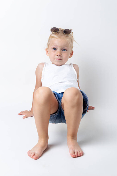 Blond child with sunglasses posing on a light background in the studio. - Foto, Bild