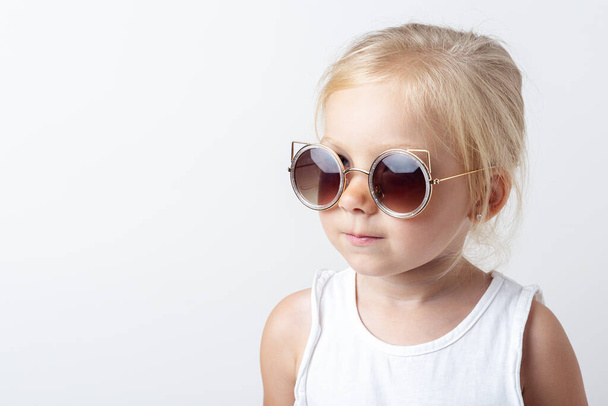 Beautiful blonde child in sunglasses on a light studio background.  - Photo, Image