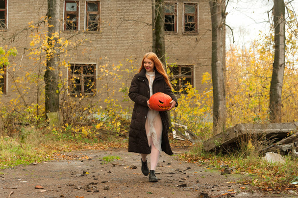 Uma menina em um feriado de Halloween caminha com uma abóbora em suas mãos. - Foto, Imagem