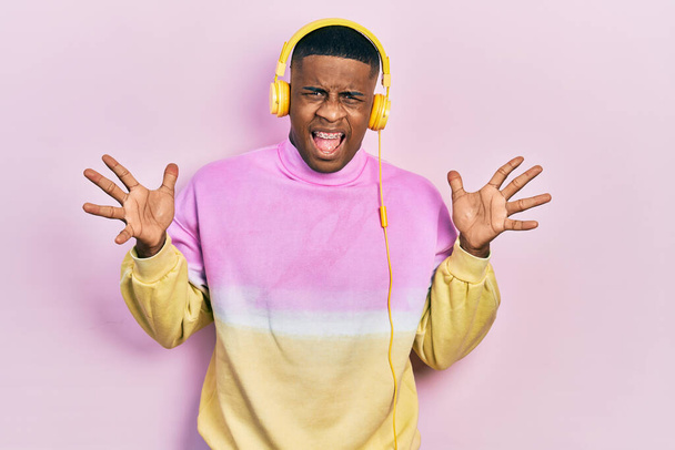Молодой черный человек слушает музыку в наушниках, празднуя безумный и безумный успех с поднятыми руками и с взволнованными закрытыми глазами. победитель концепция  - Фото, изображение