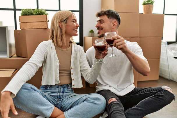 Mladý kavkazský pár přípitek s červeným vínem sklenice sedí v novém domově. - Fotografie, Obrázek