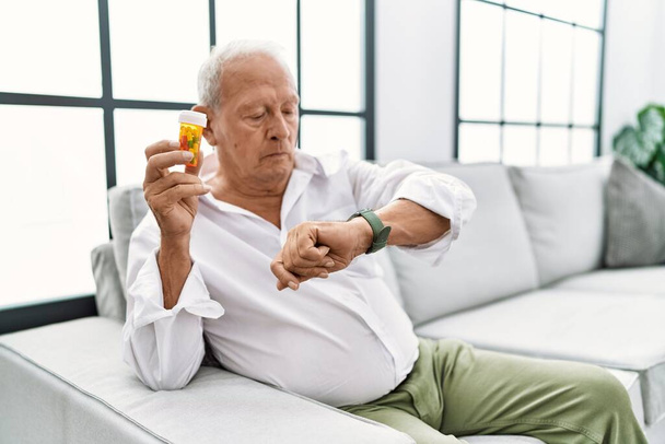Älterer Mann mit Tabletten kontrolliert die Uhrzeit an der Armbanduhr, entspannt und zuversichtlich  - Foto, Bild