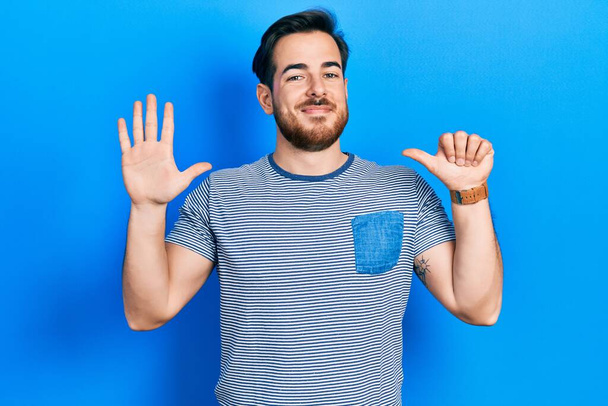 Handsome caucasian man with beard wearing casual striped t shirt showing and pointing up with fingers number six while smiling confident and happy.  - Photo, Image