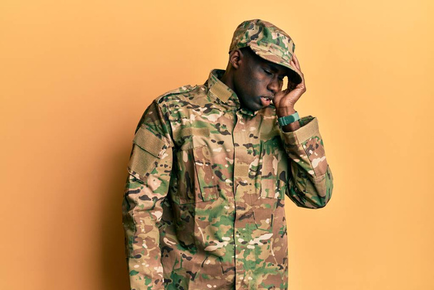 Молодий афроамериканець у військовій уніформі позіхає, закриваючи половину обличчя, очі та рот рукою. Біль завдає болю.  - Фото, зображення