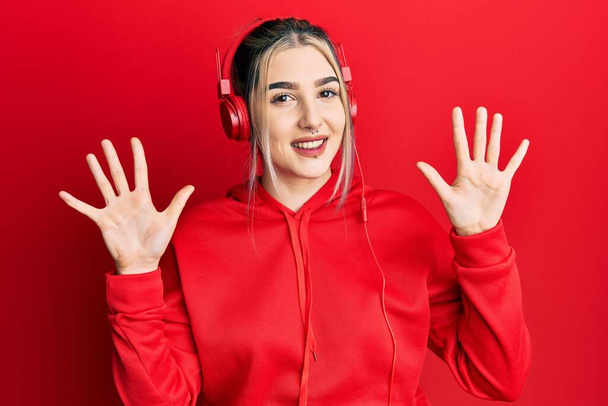 Молода сучасна дівчина носить спортивний одяг і використовує навушники, показуючи і вказуючи пальцями номер десять, посміхаючись впевнено і щасливо
.  - Фото, зображення