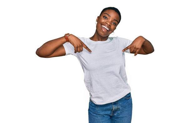 Mladý africký Američan žena na sobě ležérní bílé tričko vypadá sebevědomě s úsměvem na tváři, ukazuje se s prsty hrdý a šťastný.  - Fotografie, Obrázek