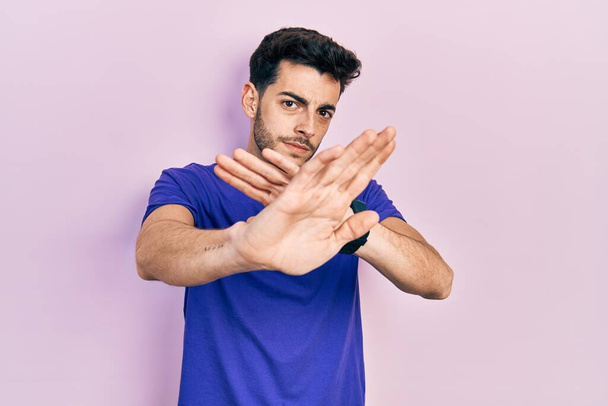 Hombre hispano joven con expresión de rechazo casual camiseta cruzando brazos haciendo signo negativo, cara enojada  - Foto, imagen