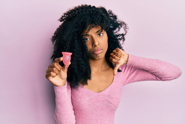 African american woman with afro hair holding menstrual cup with angry face, negative sign showing dislike with thumbs down, rejection concept  - Fotografie, Obrázek