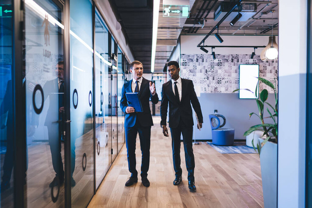Male managing director in formal suit giving tour around stylish office centre new African American hire while telling about official powers - Fotoğraf, Görsel
