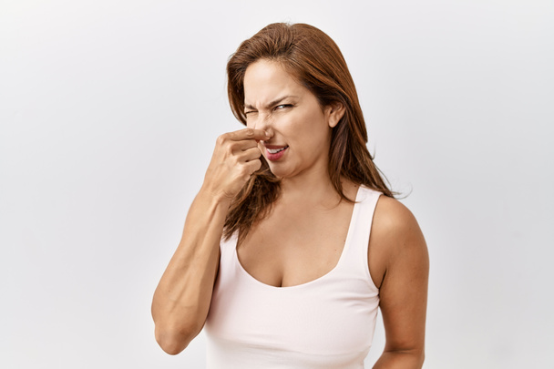 Keski-ikä latino nainen seisoo eristetty tausta haisee jotain haiseva ja vastenmielinen, sietämätön haju, pidätellen hengitystä sormet nenällä. paha haju  - Valokuva, kuva