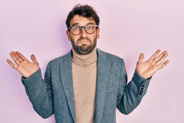 Handsome man with beard wearing business jacket and glasses clueless and confused with open arms, no idea and doubtful face.  - Photo, Image
