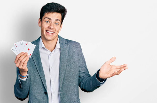 Young hispanic business man playing poker holding cards celebrating achievement with happy smile and winner expression with raised hand  - Foto, immagini