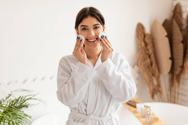 Mujer posando con almohadillas de algodón haciendo cuidado facial en el baño - Foto, imagen