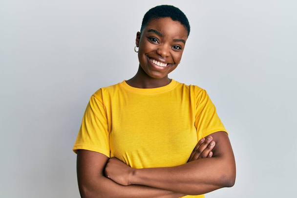 Mladá Afroameričanka v neformální žluté tričko se šťastným úsměvem se zkříženýma rukama dívá do kamery. pozitivní osoba.  - Fotografie, Obrázek