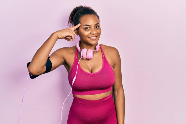 Young african american girl wearing gym clothes and using headphones smiling pointing to head with one finger, great idea or thought, good memory  - Photo, Image