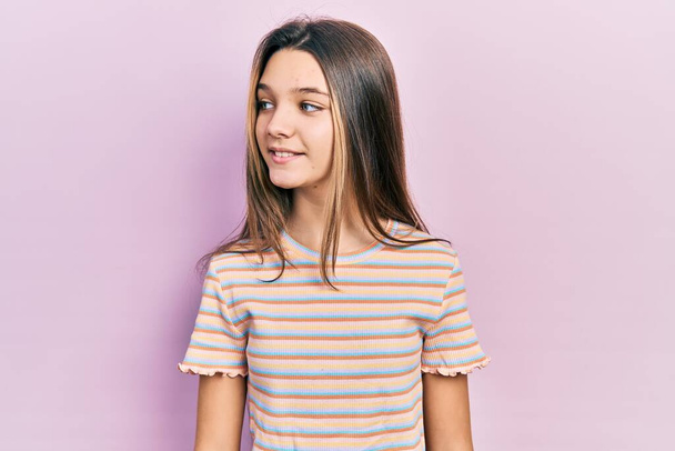 Young brunette girl wearing casual striped t shirt looking to side, relax profile pose with natural face and confident smile.  - Zdjęcie, obraz