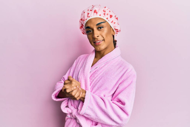Hispanic man wearing make up wearing shower towel cap and bathrobe with hands together and crossed fingers smiling relaxed and cheerful. success and optimistic  - Φωτογραφία, εικόνα