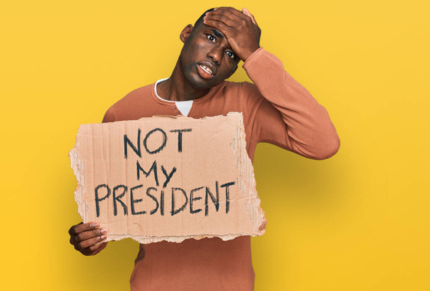 Junger afrikanisch-amerikanischer Mann, der nicht mein Präsident Protestbanner in der Hand hält, gestresst und frustriert mit der Hand auf dem Kopf, überrascht und wütend  - Foto, Bild