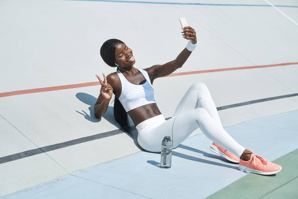 Beautiful young African woman in sports clothing having video call and smiling - Foto, imagen