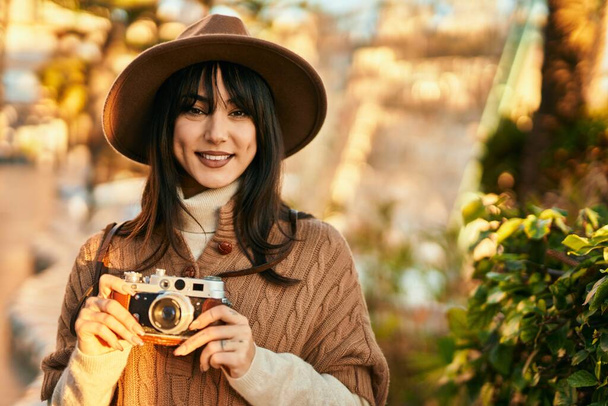 Brunetka kobieta w czapce zimowej uśmiecha się przy użyciu zabytkowej kamery w parku - Zdjęcie, obraz