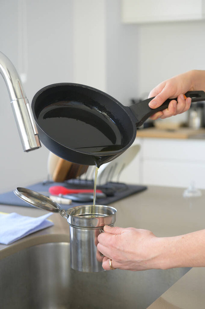 Pouring used cooking oil from an old frying pan into a metal cooking container in her kitchen.Oil recycling concept - Foto, imagen