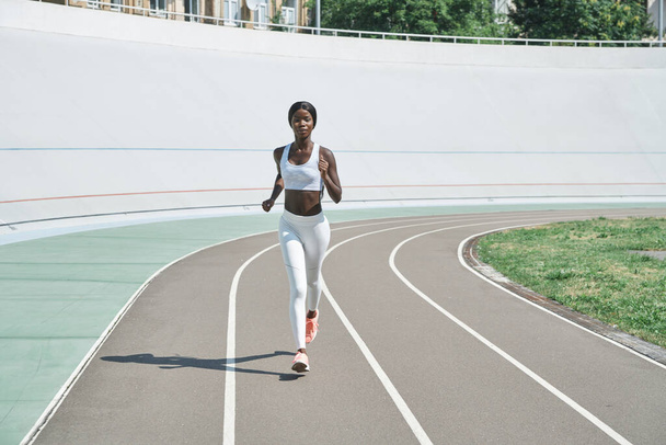 Full length of beautiful young African woman in sports clothing running on track outdoors - Fotoğraf, Görsel