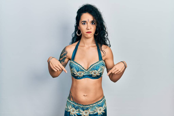 Young woman wearing bindi and traditional belly dance clothes pointing down looking sad and upset, indicating direction with fingers, unhappy and depressed.  - Photo, Image
