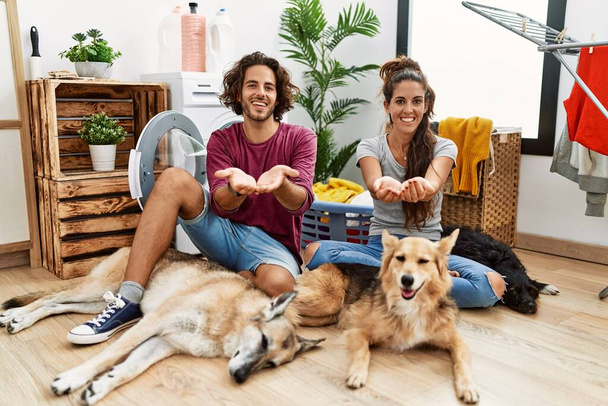 Young hispanic couple doing laundry with dogs smiling with hands palms together receiving or giving gesture. hold and protection  - Foto, Imagen