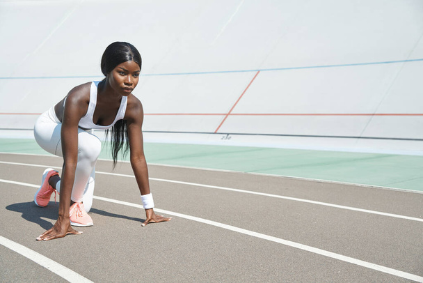 Beautiful young African woman standing at starting position on running track outdoors - Photo, Image