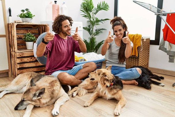Jong Latijns echtpaar doet de was met honden wijzende vingers naar de camera met een vrolijk en grappig gezicht. goede energie en vibes.  - Foto, afbeelding