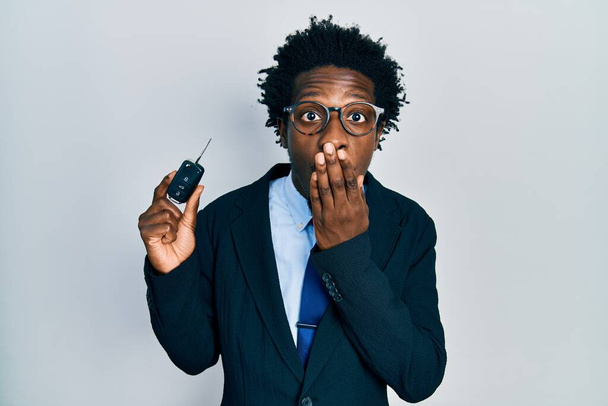 Young african american man holding key of new car covering mouth with hand, shocked and afraid for mistake. surprised expression  - Photo, Image
