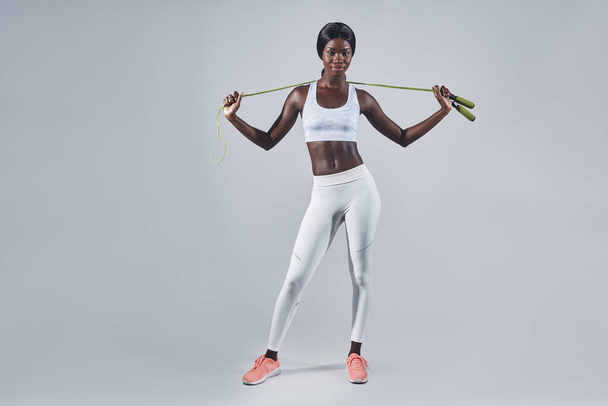 Confident young African woman in sports clothing carrying jumping rope on shoulders - 写真・画像