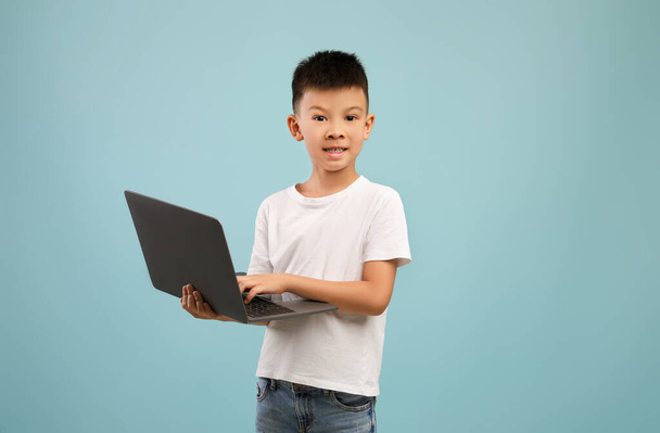 Online Education Concept. Little Asian Boy With Laptop Posing Over Blue Background - 写真・画像