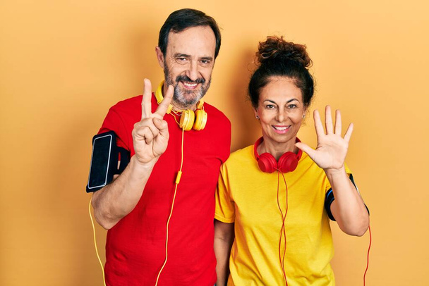 Couple d'âge moyen de femme hispanique et d'homme portant des vêtements de sport et une bande de bras montrant et pointant vers le haut avec les doigts numéro sept tout en souriant confiant et heureux.  - Photo, image