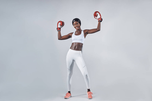 Beautiful young African woman in boxing gloves keeping arms raised - 写真・画像