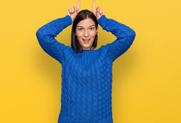 Молода іспаномовна жінка в повсякденному одязі робить смішний жест з пальцем над головою як бульбашкові роги
  - Фото, зображення