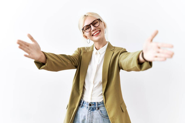 Beautiful caucasian business woman standing over isolated background looking at the camera smiling with open arms for hug. cheerful expression embracing happiness.  - Foto, imagen