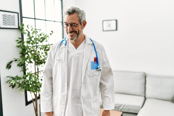 Moyen Age hispanique homme portant uniforme de médecin et stéthoscope à la salle d'attente clin d'oeil en regardant la caméra avec expression sexy, gai et heureux visage.  - Photo, image