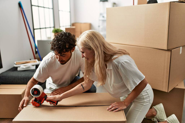 Young beautiful couple smiling happy packing cardboard box at new home. - Photo, Image