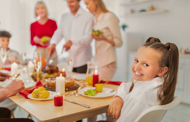 Adorável menina feliz sentada na mesa festiva, celebrando férias tradicionais com sua grande família em casa, espaço de cópia - Foto, Imagem
