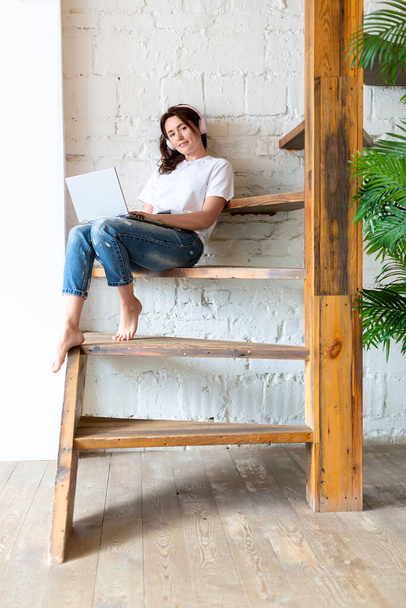 Foto vertical. de una mujer joven está sentado en una escalera de madera con un ordenador portátil. - Foto, Imagen
